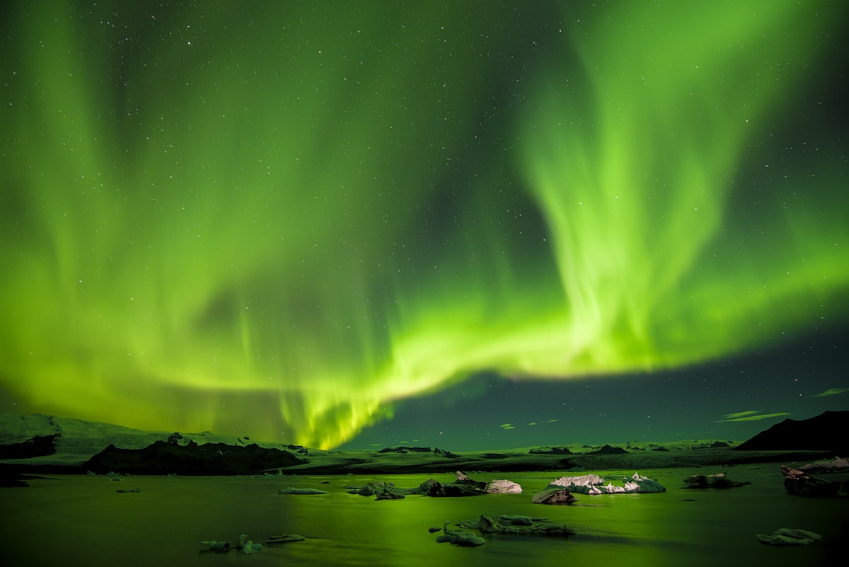 Green northern lights dancing above a rocky Icelandic coastline with the dark sea in the foreground under a clear night sky