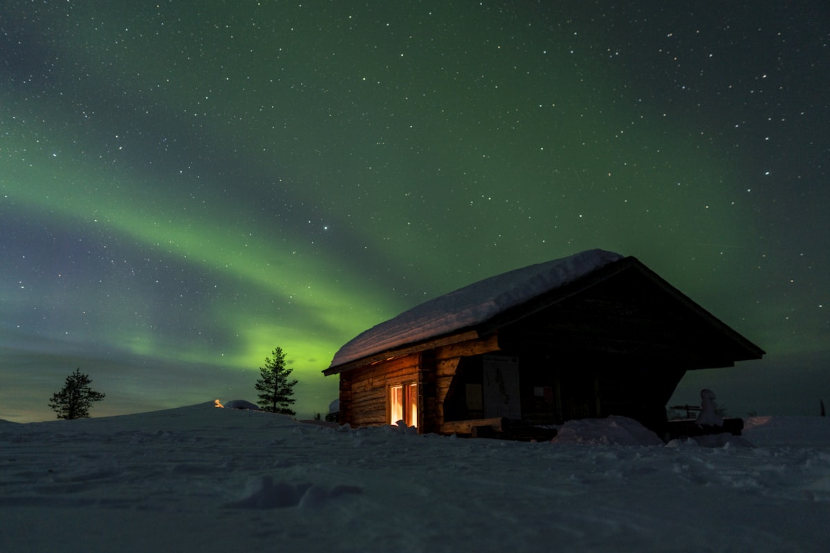 Une petite cabane à la porte éclairée, posée dans la neige profonde sous une aurore verte et un ciel criblé d'étoiles : tout l'intérêt d'un hébergement sous ciel noir en une seule image.