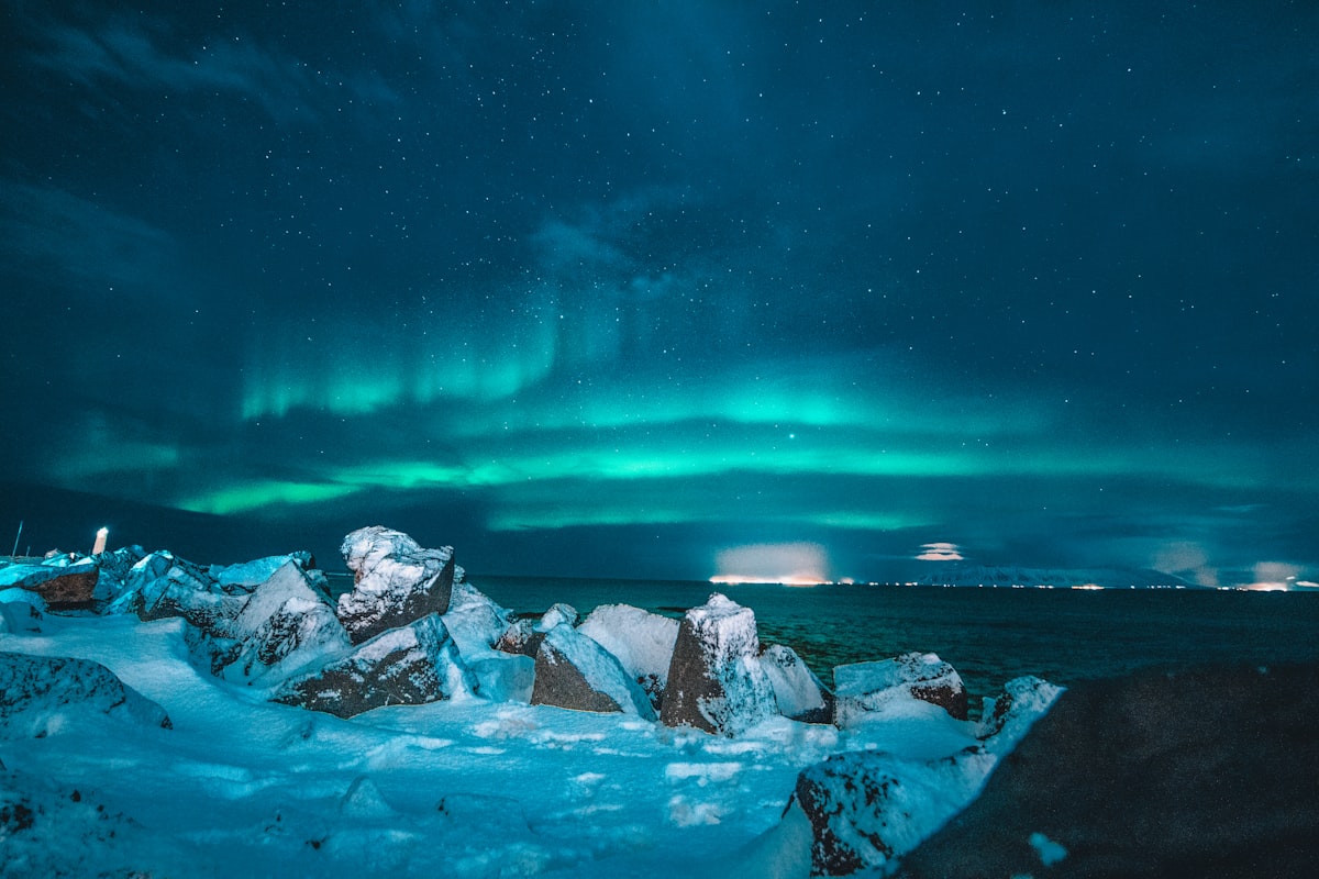 A broad green aurora arc spread across a star-filled Icelandic night sky over a dark, open landscape.
