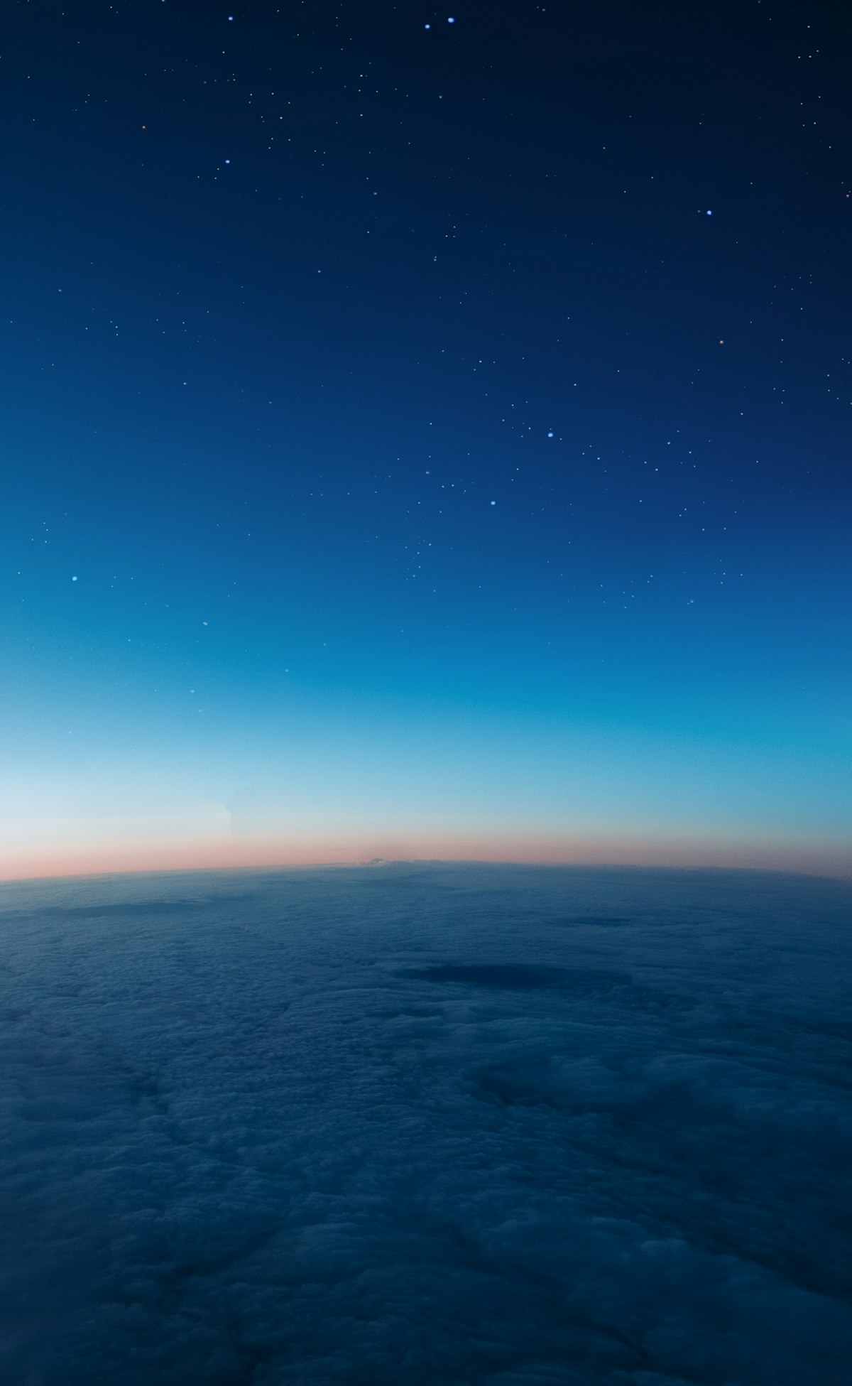 The view from cruising altitude: an unbroken deck of cloud below, a thin band of twilight along the horizon, and stars in the deep blue sky above it.