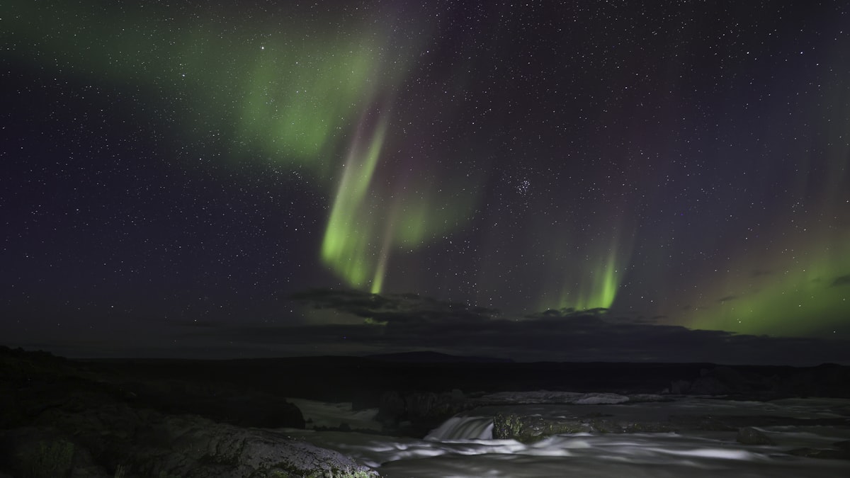 The aurora spread across the night sky above an Icelandic river, filling far more of the sky than any single window could frame.