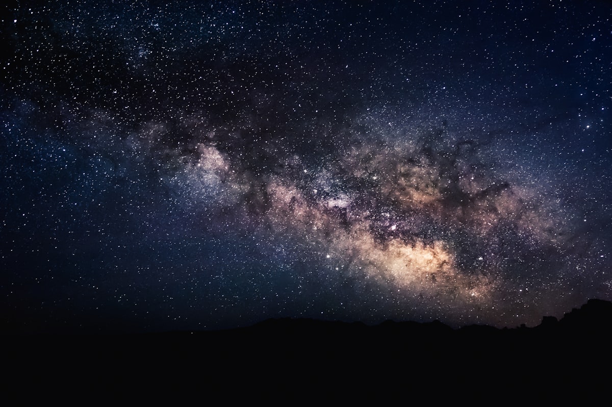 Green aurora arcing across a star-filled night sky above a dark, empty landscape.