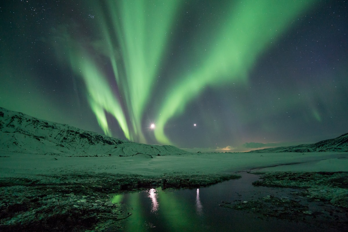 Bright green aurora borealis twisting above a dark Icelandic mountain ridge on a clear winter night.