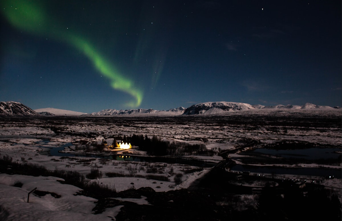 Northern lights dancing in vivid green and purple across the night sky above a dark Icelandic landscape, stars visible overhead