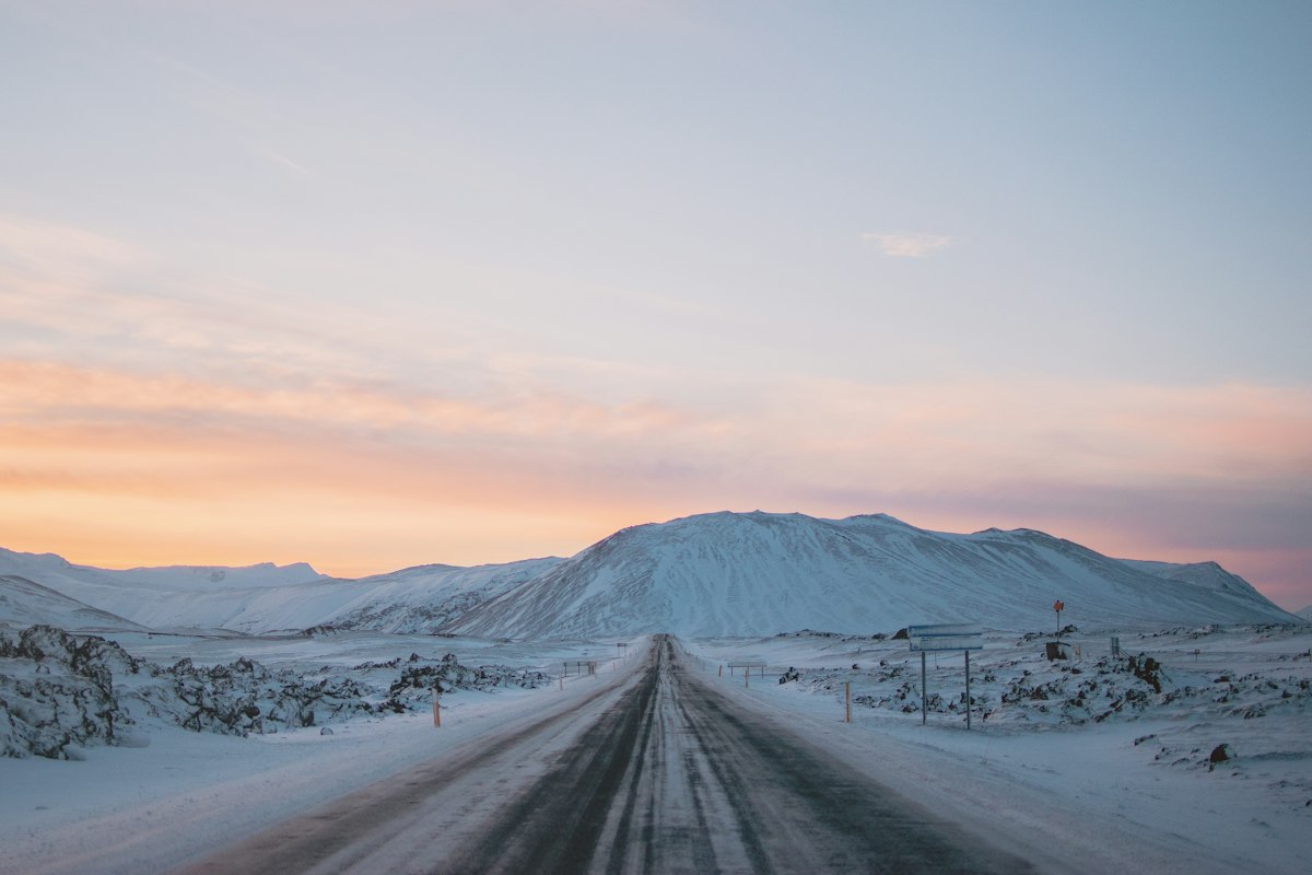 A snow-covered road stretching toward mountains on the Snaefellsnes peninsula in west Iceland, lit by the soft pastel light of a winter dusk.