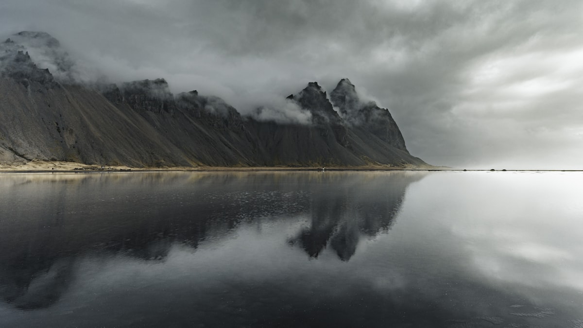 The jagged peaks of Vestrahorn mountain reflected in a shallow sheet of water on the black sand at Stokksnes, southeast Iceland.