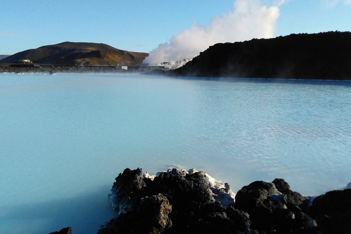 De la vapeur s'élève de l'eau bleu pâle du Blue Lagoon, avec la centrale géothermique de Svartsengi et les crêtes de lave derrière