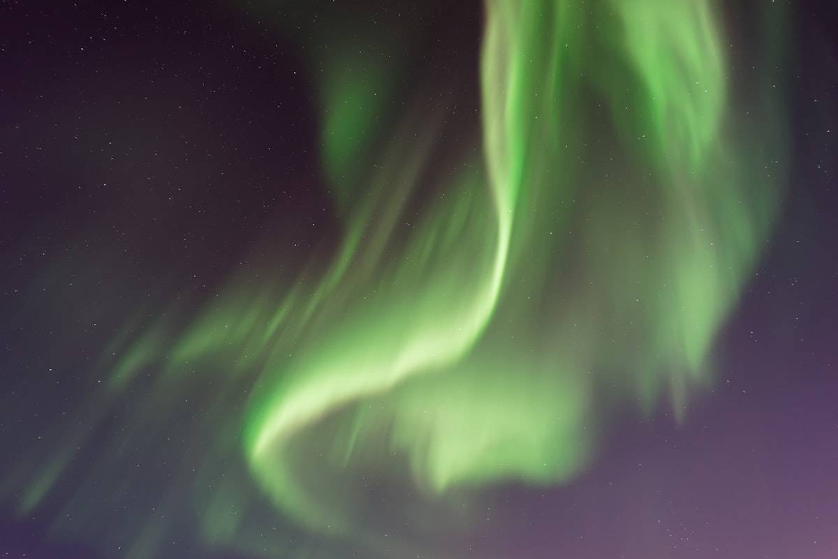 A green and faintly purple aurora spreading across a dark Icelandic sky, the kind of display that becomes visible once real darkness returns at the end of August.
