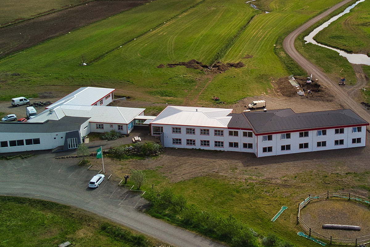 Aerial view of the Brunnhóll farm complex among green fields, with a track and river running past