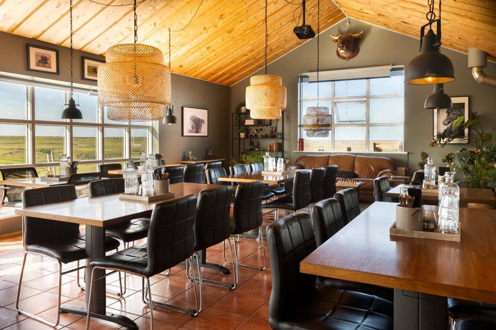 The dining room at Hestheimar, with long wooden tables, black leather chairs, woven pendant lamps and windows onto the fields