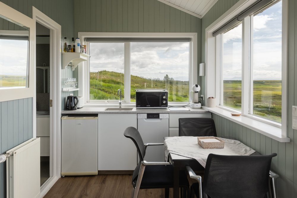 The kitchenette in a Hestheimar cottage: a small kitchen, a table for four and windows looking out over the plains