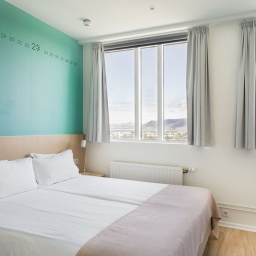 A twin room at Reykjavik Lights, with a teal calendar wall and tall windows looking out to the mountains