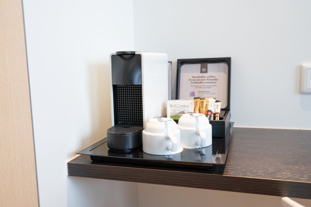 A capsule coffee machine, two white cups and a tray of tea and coffee sachets on a dark shelf in a Reykjavik Lights room