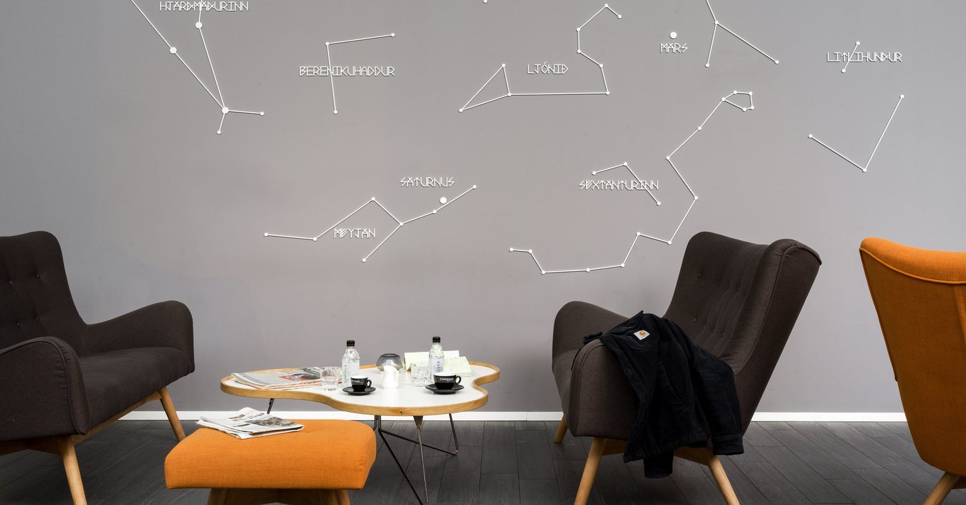 Two dark armchairs and an orange footstool around a low table in the Reykjavik Lights lounge, under a wall-sized star map with the constellations named in Icelandic