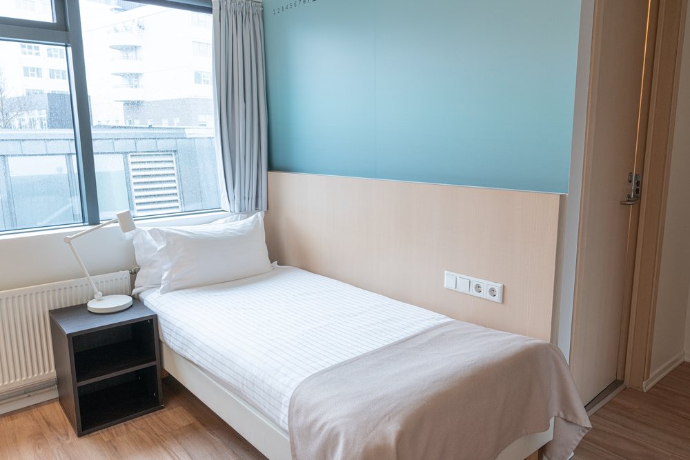 A single room at Reykjavik Lights: one bed by the window, a lamp on a dark bedside table and a teal wall