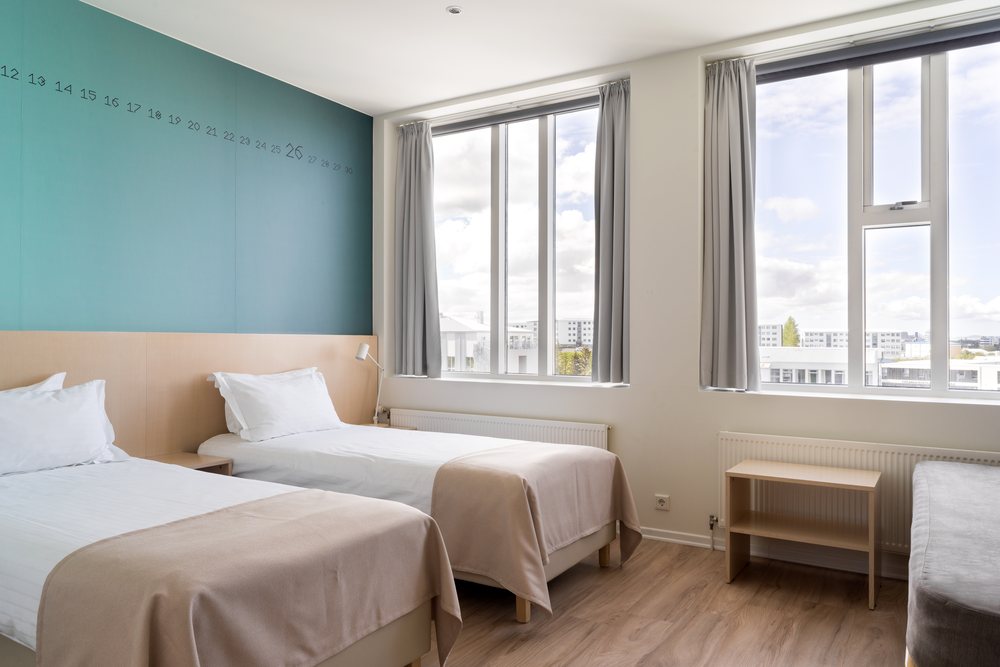 A triple room at Reykjavik Lights with two beds under a teal calendar wall and windows on two sides