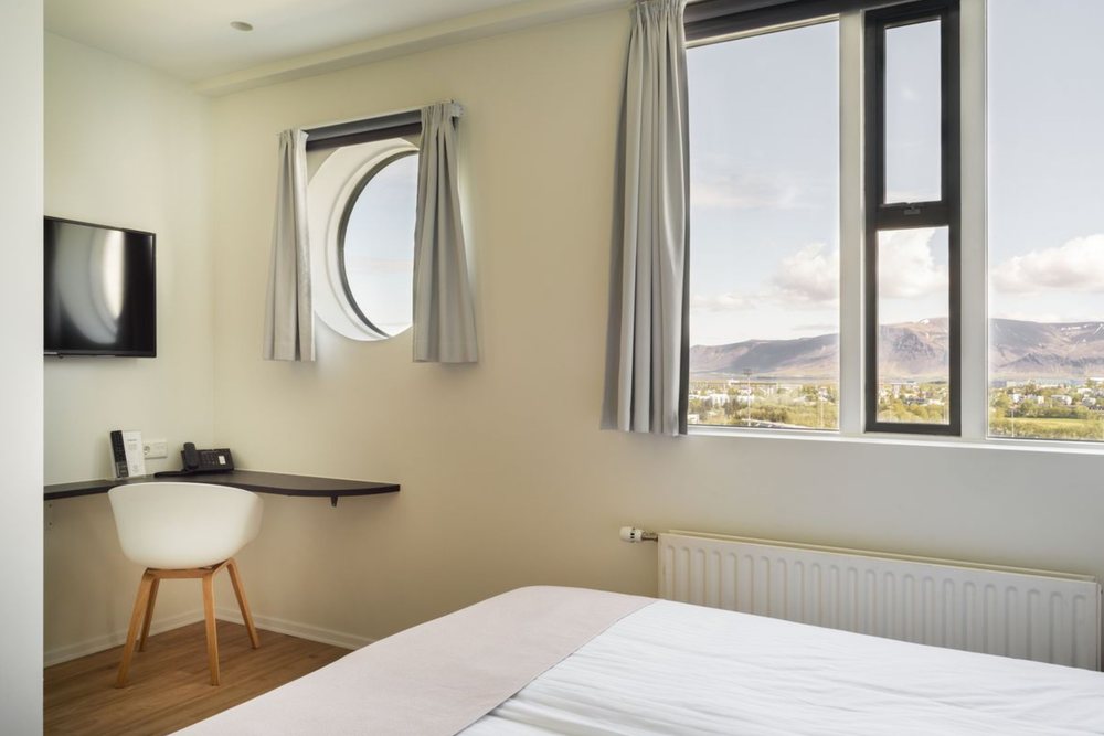 A 7th-floor mountain-view room at Reykjavik Lights, with a round porthole window and tall windows looking north over the city to Mt. Esja