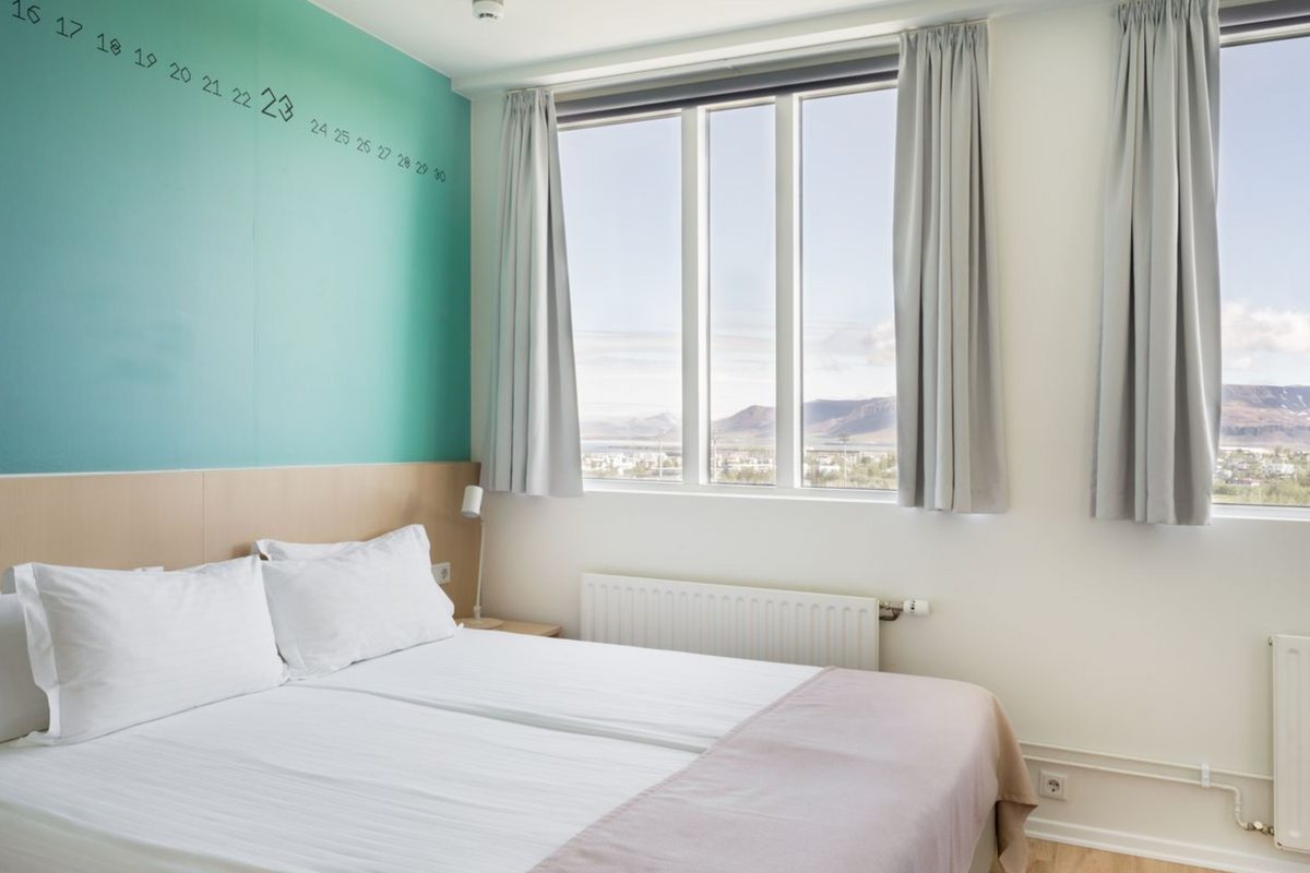 A twin room at Reykjavik Lights, with a teal wall lettered with the days of an old Icelandic month and tall windows looking out over the city to the mountains